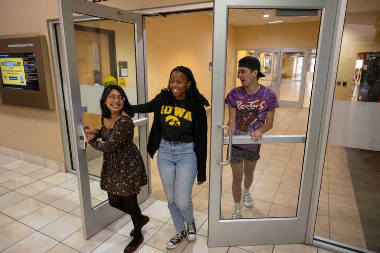 Students laughing leaving through glass door vestibule 
